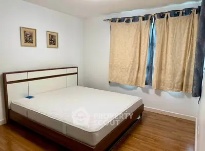 Spacious bedroom with wooden flooring and large window, perfect for comfort and relaxation.