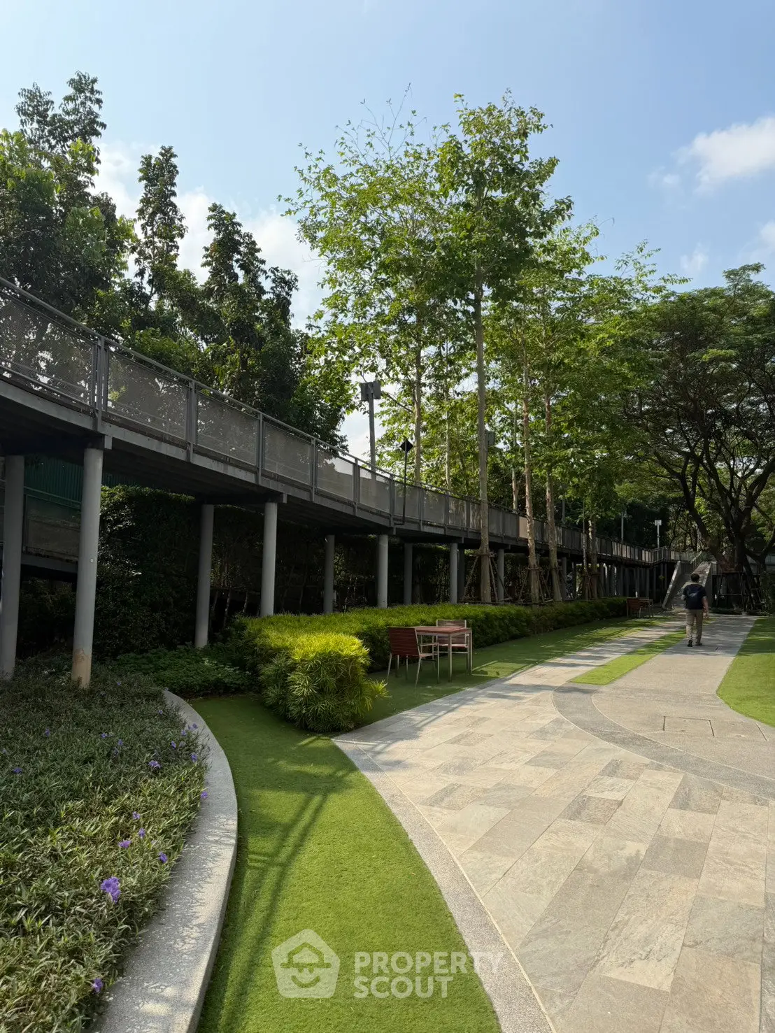 Lush garden pathway with elevated walkway and seating area in modern residential complex.