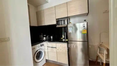 Modern kitchen with sleek cabinets, stainless steel fridge, and washing machine in compact layout.