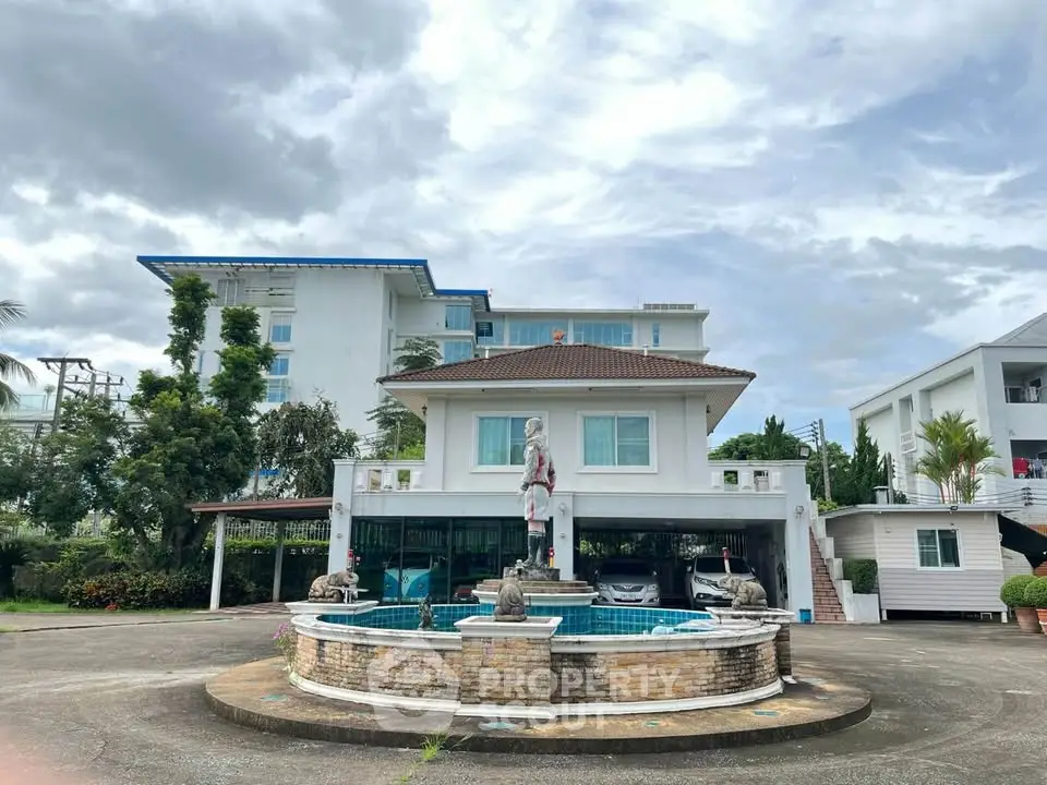 Stunning two-story house with a fountain in a spacious driveway, surrounded by lush greenery and modern architecture.