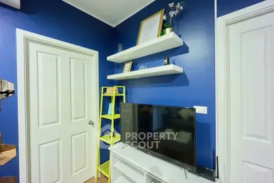 Charming living room with blue walls, modern TV setup, and stylish shelving for a cozy ambiance.