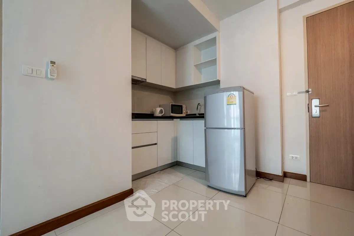 Modern compact kitchen with fridge, microwave, and sleek cabinetry in a cozy apartment.