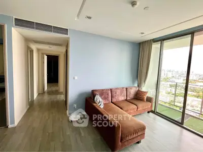 Modern living room with large windows and city view, featuring a stylish brown sofa and light wood flooring.