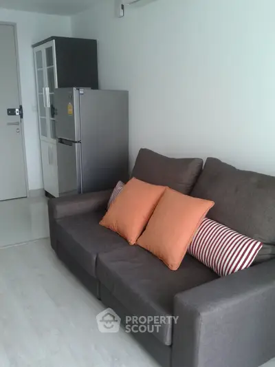 Modern living room with sleek sofa and stainless steel fridge in a compact apartment setting.