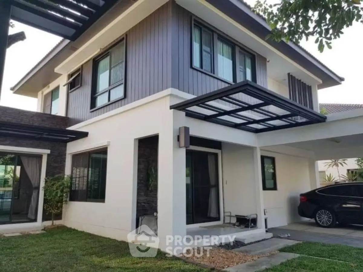 Modern two-story house with carport and landscaped garden, featuring sleek architectural design and large windows.