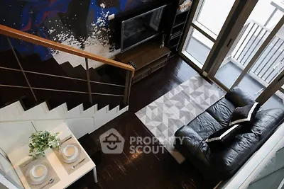 Modern living room with stylish decor, featuring a black leather sofa, geometric rug, and artistic wall design.