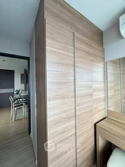 Modern apartment interior with sleek wooden wardrobe and dining area in view.