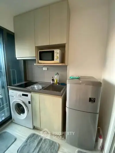 Compact modern kitchen with washing machine, microwave, and fridge in cozy apartment.