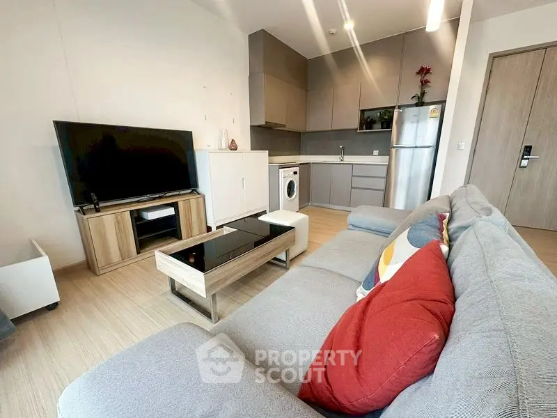 Modern living room with stylish furniture and open kitchen layout, featuring a washing machine and sleek appliances.