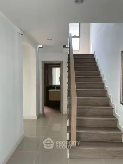 Modern staircase with sleek wooden steps and glossy tiled floor in a bright hallway.
