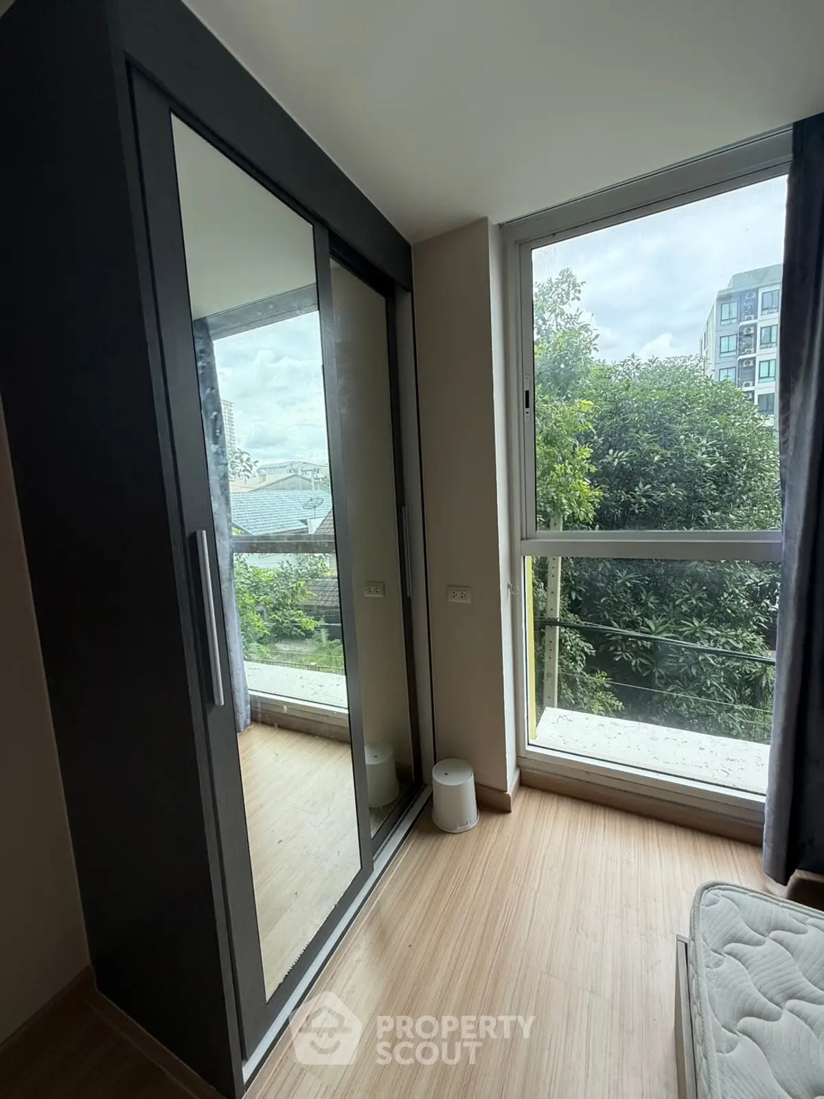 Bright bedroom with large window and mirrored wardrobe offering lush green views.
