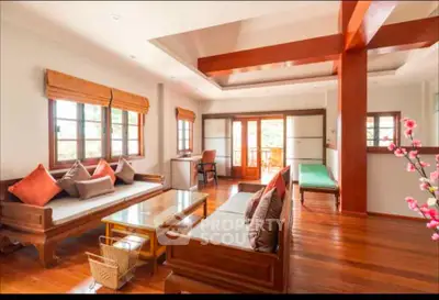 Spacious living room with wooden flooring and elegant furniture, featuring large windows and natural light.