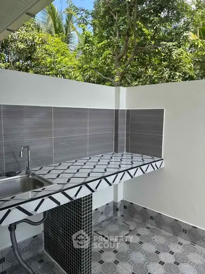 Charming outdoor kitchen with tiled countertop and lush greenery backdrop.