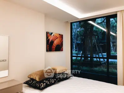 Modern bedroom with large window and stylish decor overlooking a lush garden view.