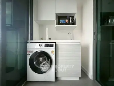 Modern compact kitchen with washing machine and microwave in sleek apartment.