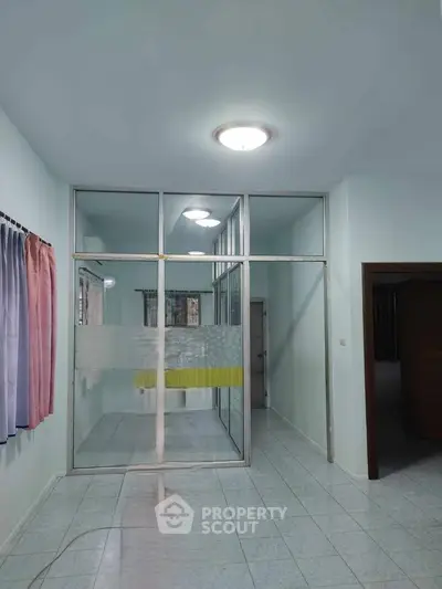 Spacious interior with glass partition and tiled flooring, ideal for versatile living space.