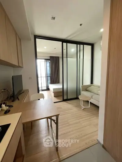 Modern studio apartment with open layout, featuring a cozy living area and bedroom separated by glass partitions.