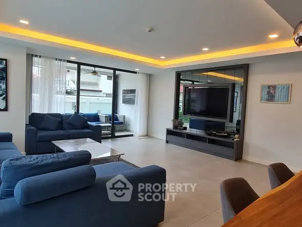 Spacious modern living room with blue sofas and large TV, featuring a balcony view.
