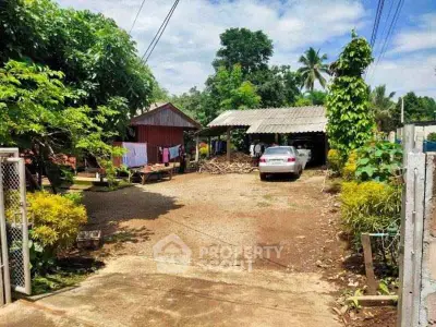 Charming rural property with spacious yard and carport, surrounded by lush greenery and traditional wooden structures.
