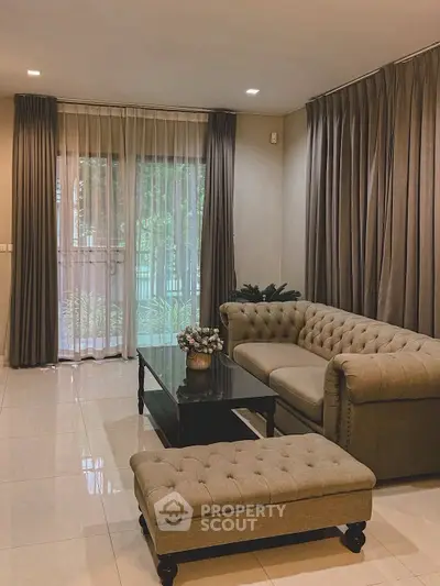 Elegant living room with plush sofa, coffee table, and large windows with curtains, offering a cozy ambiance.