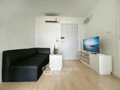 Modern living room with sleek black sofa and flat-screen TV on wooden floor.