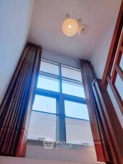 Bright interior with high ceiling and large window, elegant curtains and modern lighting fixture.