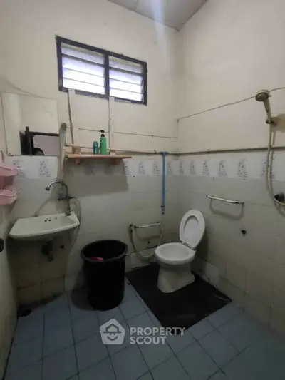 Basic bathroom with shower, toilet, and sink in a modest setting.