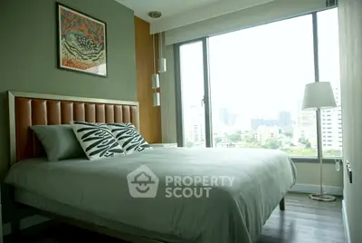 Modern bedroom with large window and city view, featuring stylish decor and comfortable bedding.