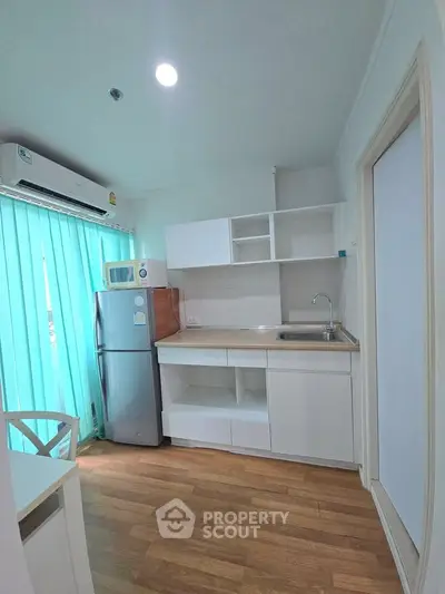 Modern kitchen with sleek white cabinets, wooden flooring, and natural light from large window.