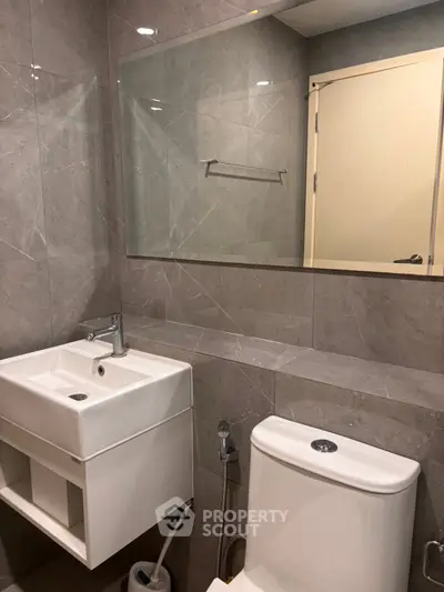 Modern bathroom with sleek fixtures and elegant gray tiles, featuring a stylish sink and toilet.