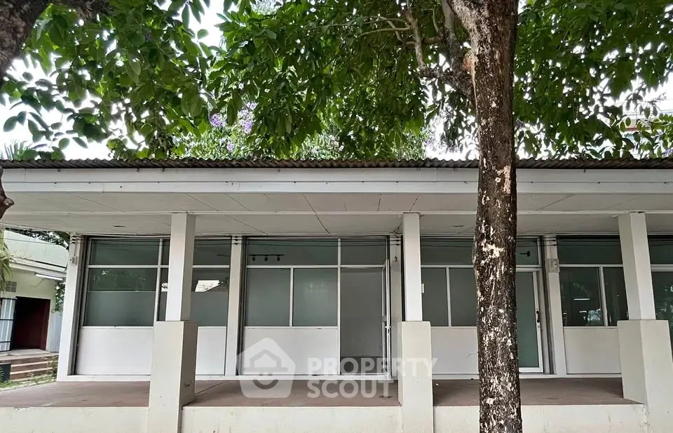 Charming single-story building with large windows and lush greenery, ideal for commercial or residential use.