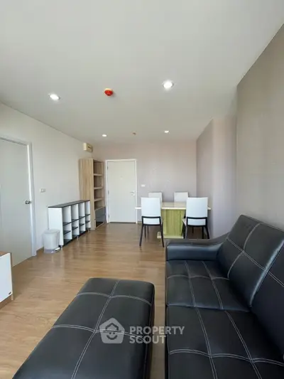 Spacious modern living room with sleek black leather furniture and wooden flooring.