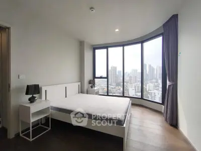 Spacious bedroom with panoramic city view and modern furnishings in high-rise apartment.