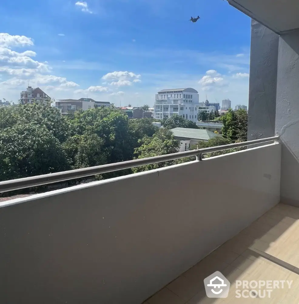 Spacious balcony with scenic city view and lush greenery under a clear blue sky.