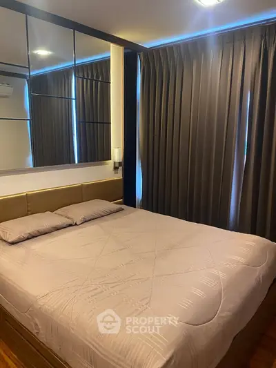 Cozy bedroom with modern decor and large bed, featuring elegant curtains and mirrored wall accents.