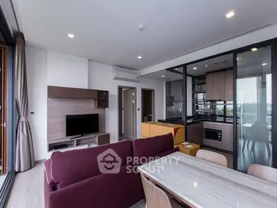 Modern open-plan living room with kitchen, featuring sleek furniture and large windows for natural light.