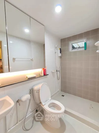 Modern bathroom with sleek fixtures and neutral tiles, featuring a shower and toilet.