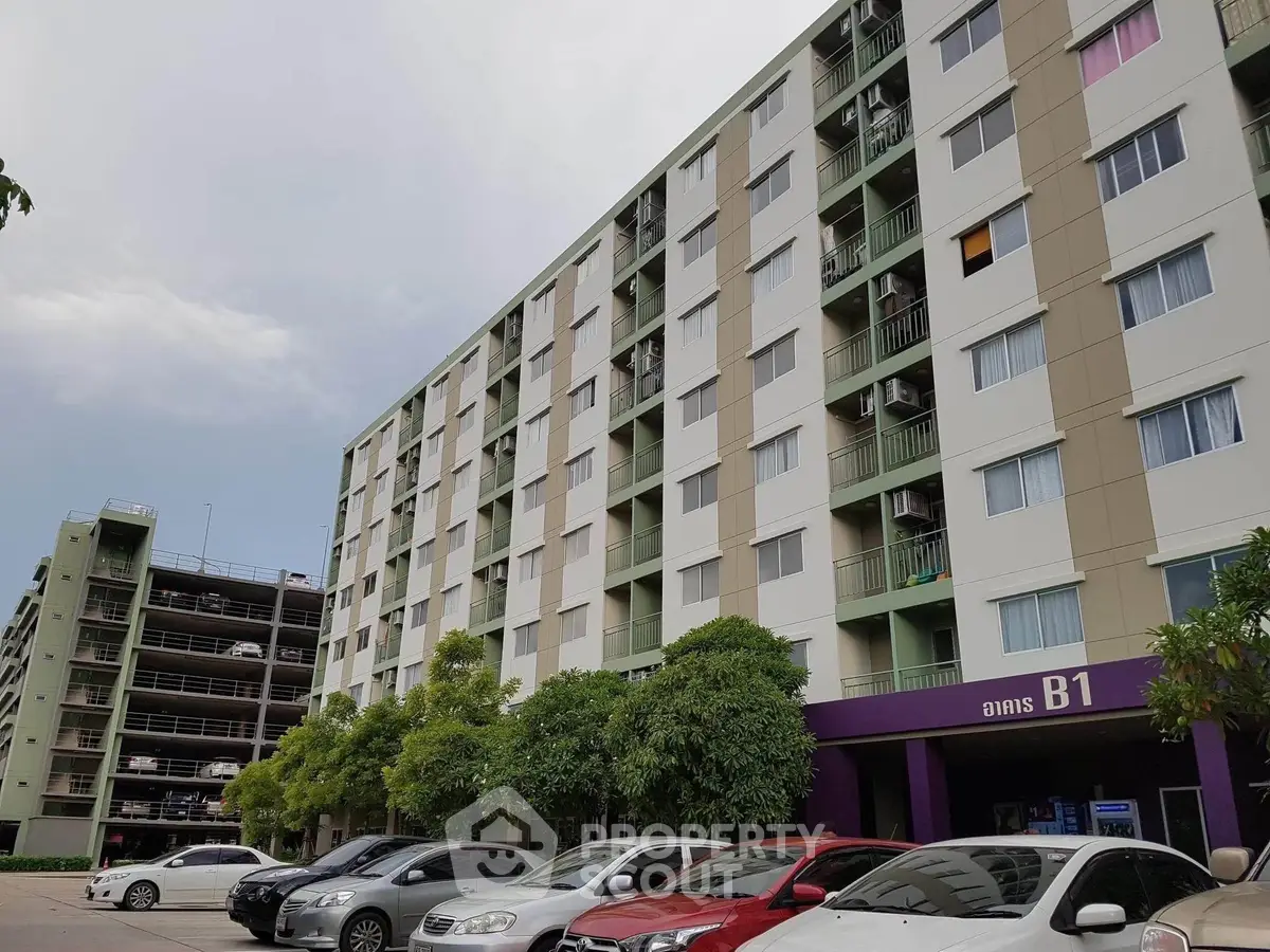 Modern multi-story apartment building with spacious parking area and lush greenery.
