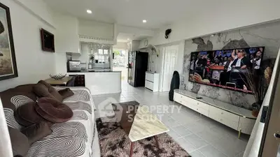 Modern living room with stylish decor and open kitchen layout, featuring a large TV and comfortable seating.