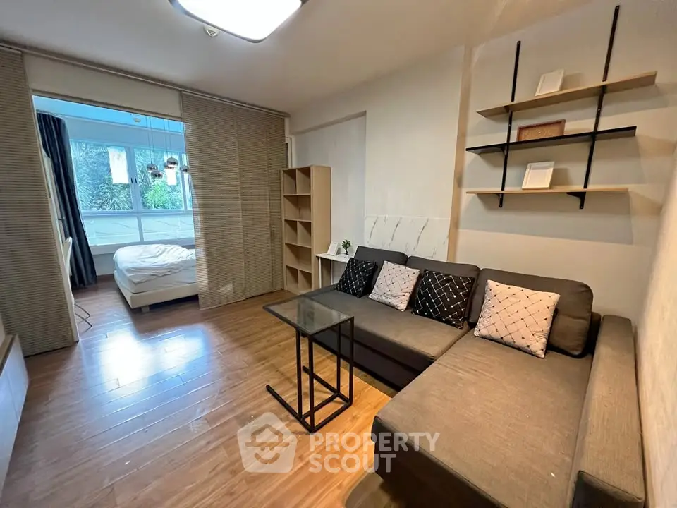 Modern living room with cozy sofa and open view to bedroom, featuring stylish shelving and wooden flooring.