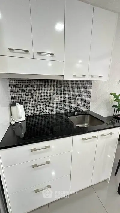 Modern kitchen with sleek white cabinets and black countertop, featuring a stylish backsplash and compact sink.