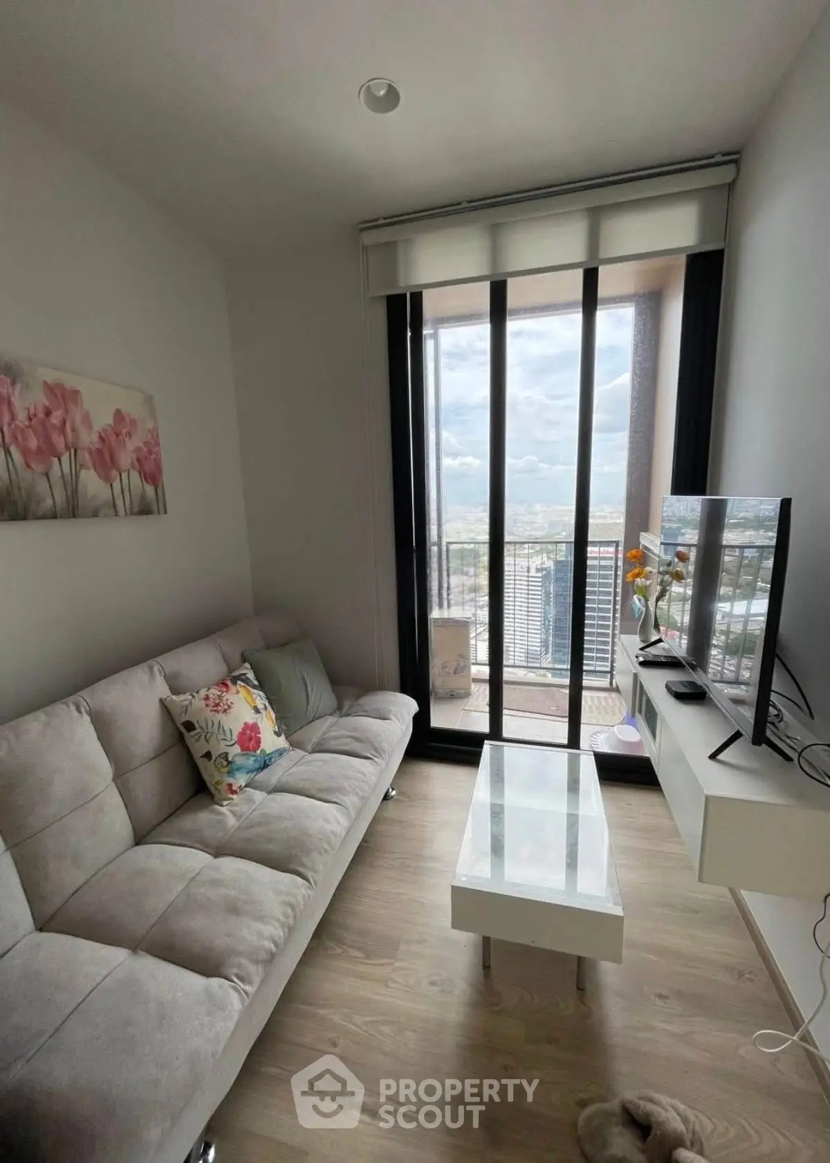 Modern living room with floor-to-ceiling windows and city view, featuring a cozy sofa and sleek TV setup.
