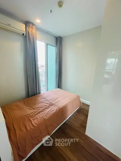 Cozy bedroom with wooden flooring and large window offering natural light and city views.