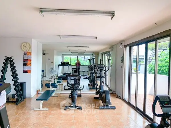 Spacious gym with modern equipment and large windows offering natural light.