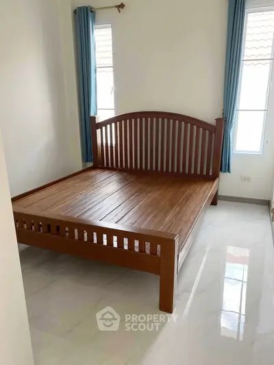 Spacious bedroom with wooden bed frame and natural light from large windows.