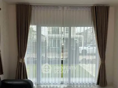 Spacious living room with large windows and elegant curtains overlooking a garden view.
