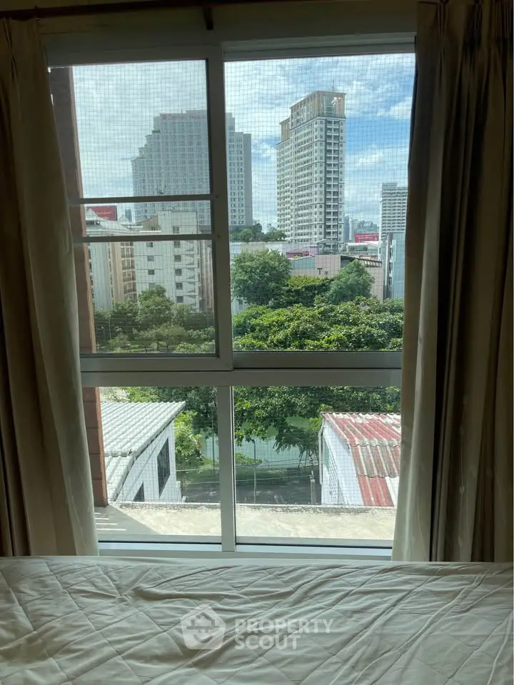 Bright bedroom with large window offering stunning cityscape view, perfect for urban living.
