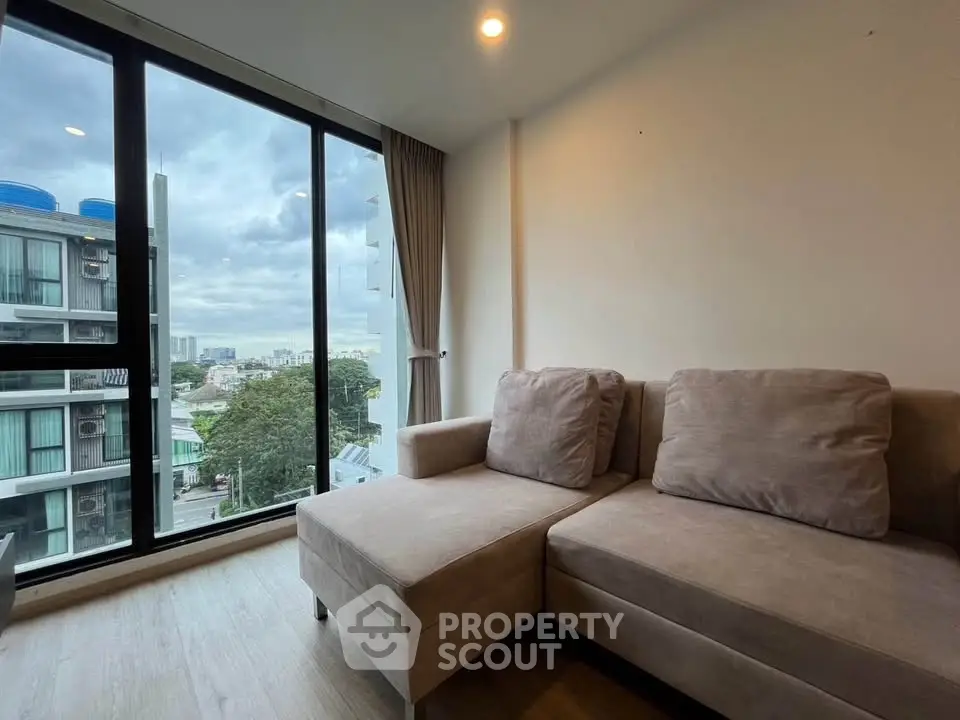 Modern living room with large windows offering a stunning city view, featuring a cozy beige sofa.