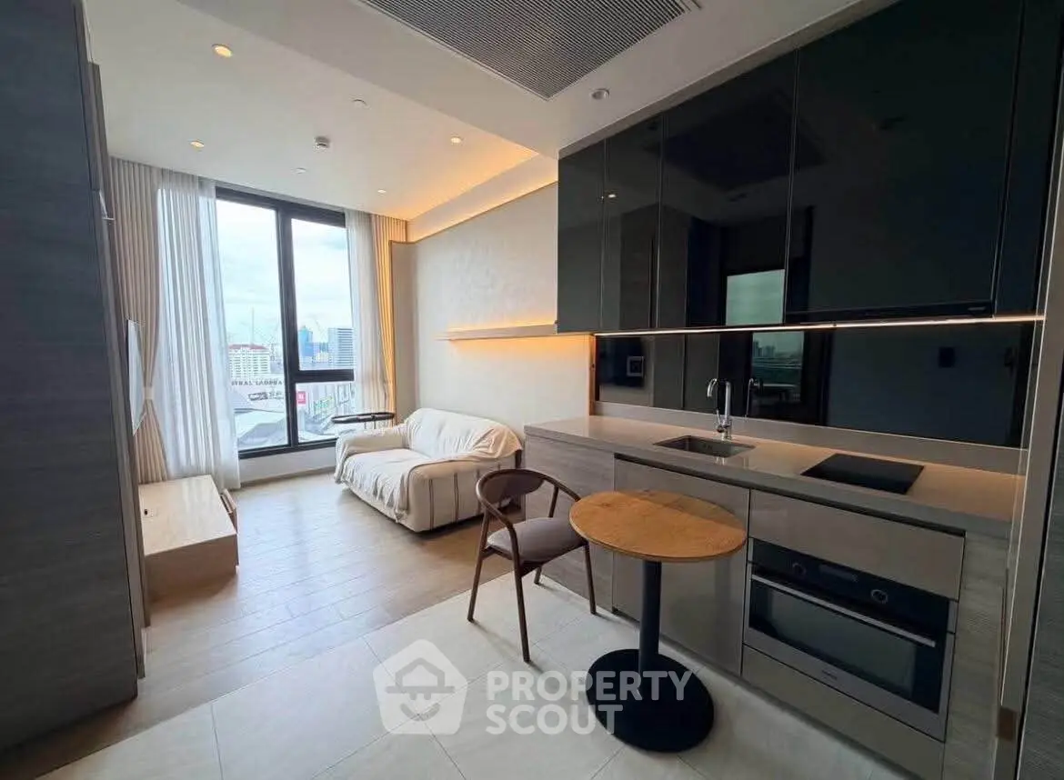 Modern open-layout living room with sleek kitchen and city view, featuring stylish furniture and ample natural light.