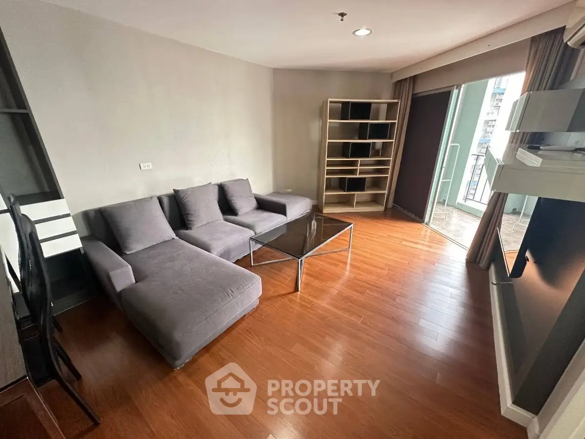Spacious living room with modern gray sofa and wooden flooring, leading to a balcony with city views.